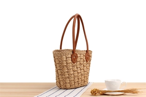 Detail of hand-woven straw bag featuring natural grid texture and brown leather handles