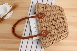 Macro view of woven straw tote bag with brown leather handles and rivet details