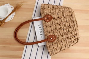 Close-up of woven straw tote bag featuring brown leather handles and rivet details
