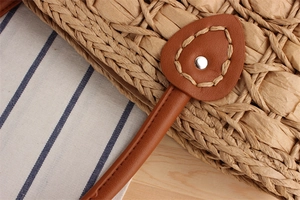 Close-up of woven straw handbag featuring leather reinforced handles and metal rivets
