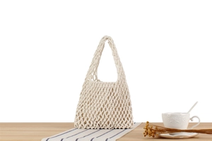Detail of handmade cream macrame woven tote bag on a rustic wooden table for vacation