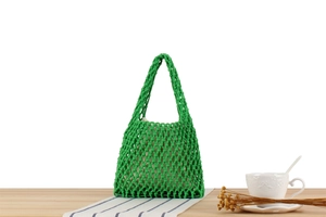 Detail of green macramé woven beach bag with beige inner pouch on wooden table