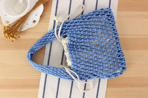 Detailed overhead view of a blue macrame woven tote with a cream drawstring pouch