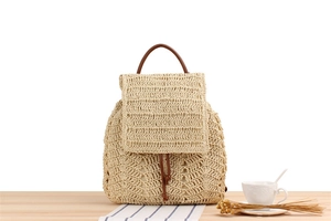 Detail of beige straw backpack featuring intricate crochet patterns and leather handle