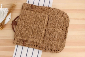 Detail of woven straw backpack with hollow crochet texture and leather handle on wood