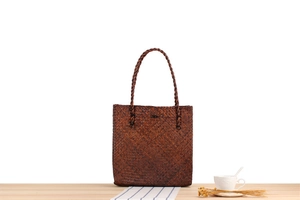 Detail of hand-woven dark brown straw tote bag with intricate texture on a wooden table