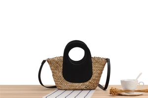 Detail of woven straw handbag with black velvet trim on a rustic wooden table