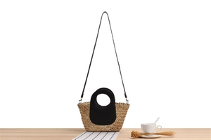 Detail of handwoven straw handbag with black round handles and detachable strap
