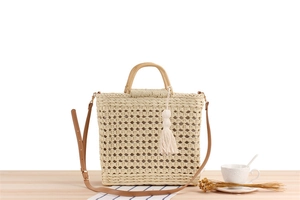 Detail of paper straw tote bag featuring wood handles, brown strap and cotton tassels