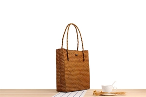 Close-up of handmade woven straw tote bag with long shoulder straps on a wooden table