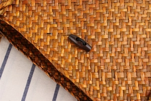Close-up of a woven straw shoulder bag featuring a vintage wooden toggle closure