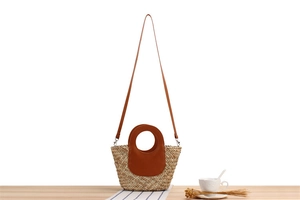 Detail of woven straw bag with brown leather handles and shoulder strap on wooden table