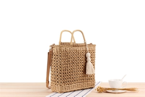 Detail of hollow-out woven straw tote with wooden handles and leather shoulder strap