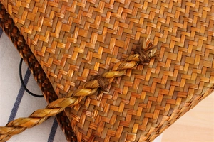 Macro detail of hand-woven straw shoulder bag showing natural fiber texture and strap