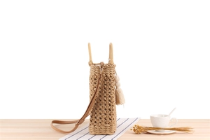 Detail of beige paper rope woven bag with wooden handles and matching tassel accessory