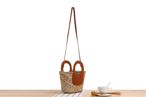 Detailed view of woven straw bucket bag with brown leather trim and matching handle