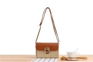 Detail of woven straw crossbody bag with brown leather flap and golden metal ring