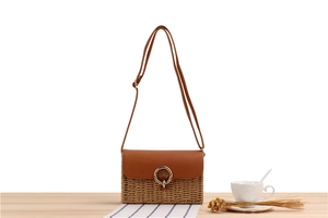 Detail of woven straw bag with faux leather flap and gold ring closure on wooden table