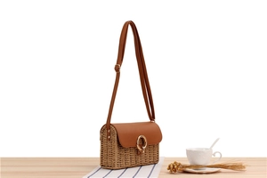 Detail of straw crossbody bag with brown leather flap and golden circular metal clasp