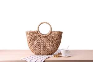 Close-up of semi-circle corn husk woven bag with round handle on a wooden surface