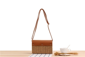 Close-up of woven straw handbag with brown leather flap and stylish metal studs detailing