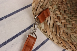 Close-up of woven straw bag texture with brown leather strap and silver metal buckle hook