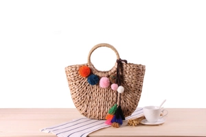 Detail of handmade straw bag featuring colorful pom-poms and tassels on a wood surface