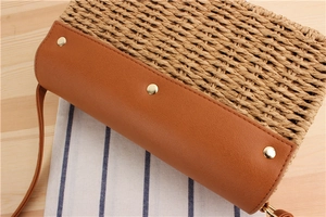 Close-up of woven straw bag with tan leather base and gold metal rivets on wooden table