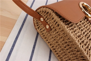 Detailed close-up of woven bag texture with brown leather flap and golden metal hardware