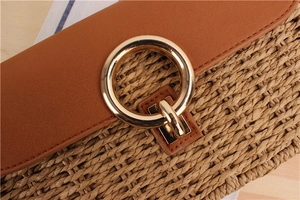 Detail of hand-woven straw bag featuring a brown leather flap and large gold metal ring buckle