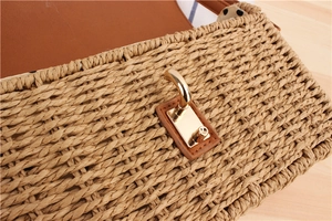 Detail view of woven straw handbag featuring a gold rectangle twist lock and brown leather