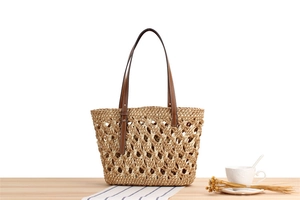Close-up of woven mesh texture and dark brown leather handle on a straw beach tote bag