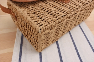 Close-up of hand-woven straw tote with premium brown leather handles and stitching