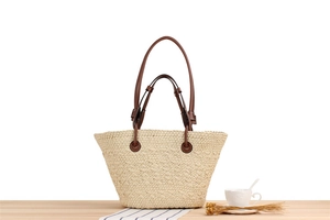 Detail of woven straw tote bag with dual brown leather handles on a wooden table