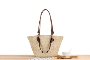 Detail of hand-woven paper rope tote bag with dark brown leather straps on a wooden table