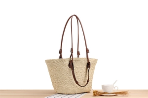 Close-up of large straw tote bag with brown leather straps on a wooden table