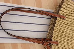 Detailed close-up of woven straw tote bag with brown leather strap and contrast stitching