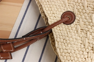 Detail of woven straw bag showing brown leather handle with silver metal eyelets