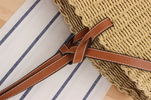Detailed shot of handmade paper straw bag featuring brown leather strap and contrast stitching