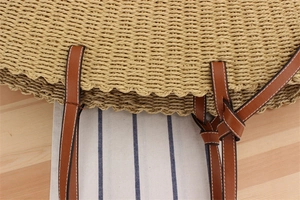 Detailed close-up of straw woven texture with brown faux leather strap and stitching