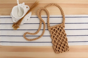 Flat lay of a beige hand-woven crossbody phone bag with a hollow design and long strap