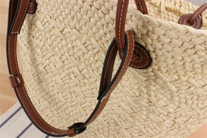 Detailed close-up of woven paper rope straw tote with brown leather strap and contrast stitching