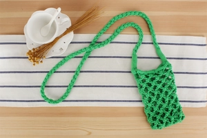 Macro shot of green handmade woven cotton phone bag on a blue striped tablecloth