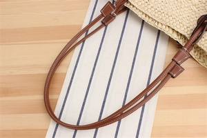 Detail of woven straw shoulder bag featuring brown leather straps with white stitching