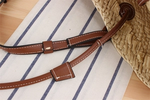 Detail of woven straw beach bag featuring brown leather strap with contrast white stitching