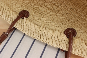 Detail of woven straw beach bag with brown leather handles and white stitching details