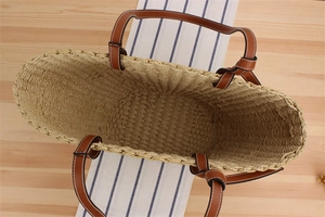 Top-down view of a spacious paper straw tote bag with brown leather handles on wood