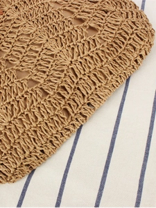 Handcrafted brown woven straw backpack with hollow crochet texture on striped fabric