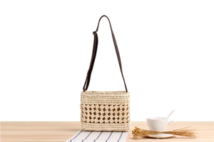 Close-up of beige woven straw crossbody bag with hollow lattice and adjustable strap