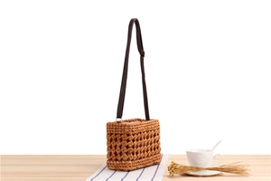 Detail of hand-woven straw crossbody bag featuring brown hollow pattern and leather strap